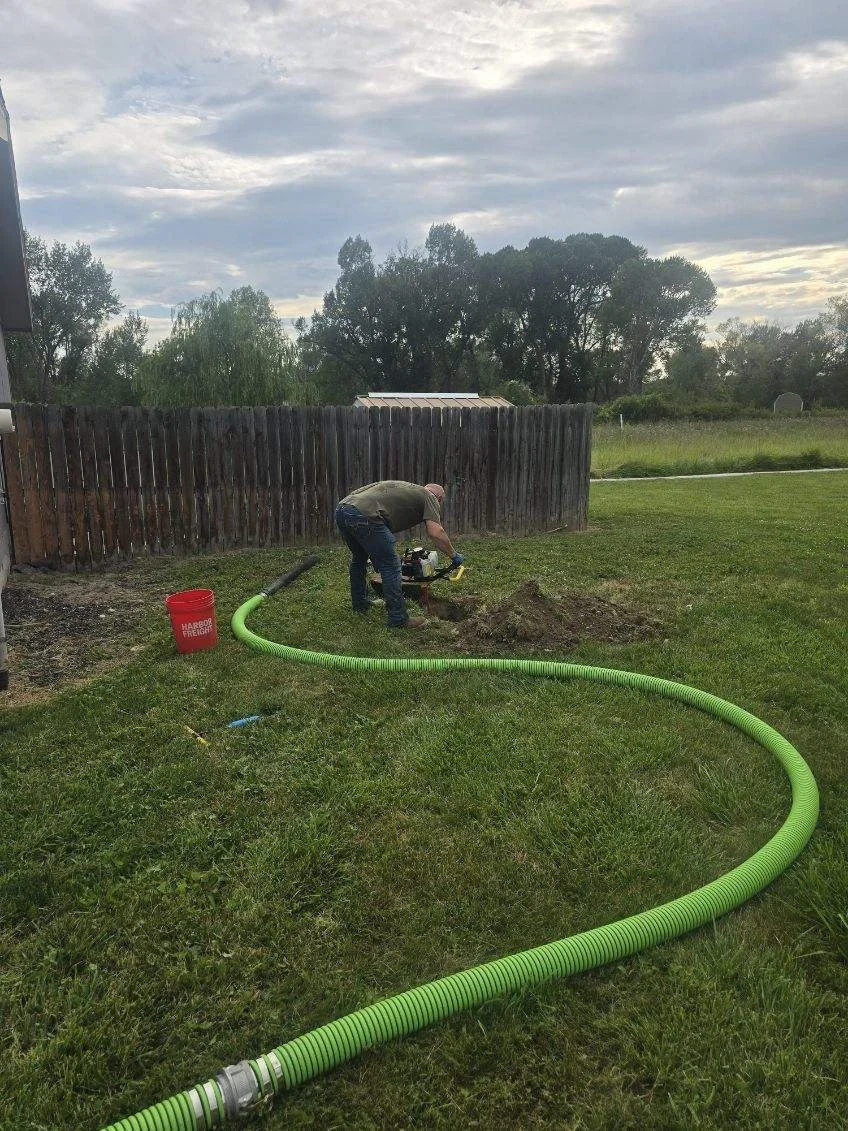 Technician installing green corrugated septic drain lines in yard with wooden fence